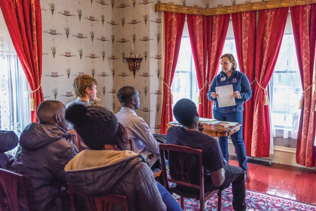 Principia College students visit the Mary Baker Eddy Historic House Lynn Massachusetts. A Longyear tour guide talks with them in the front parlor of the house.