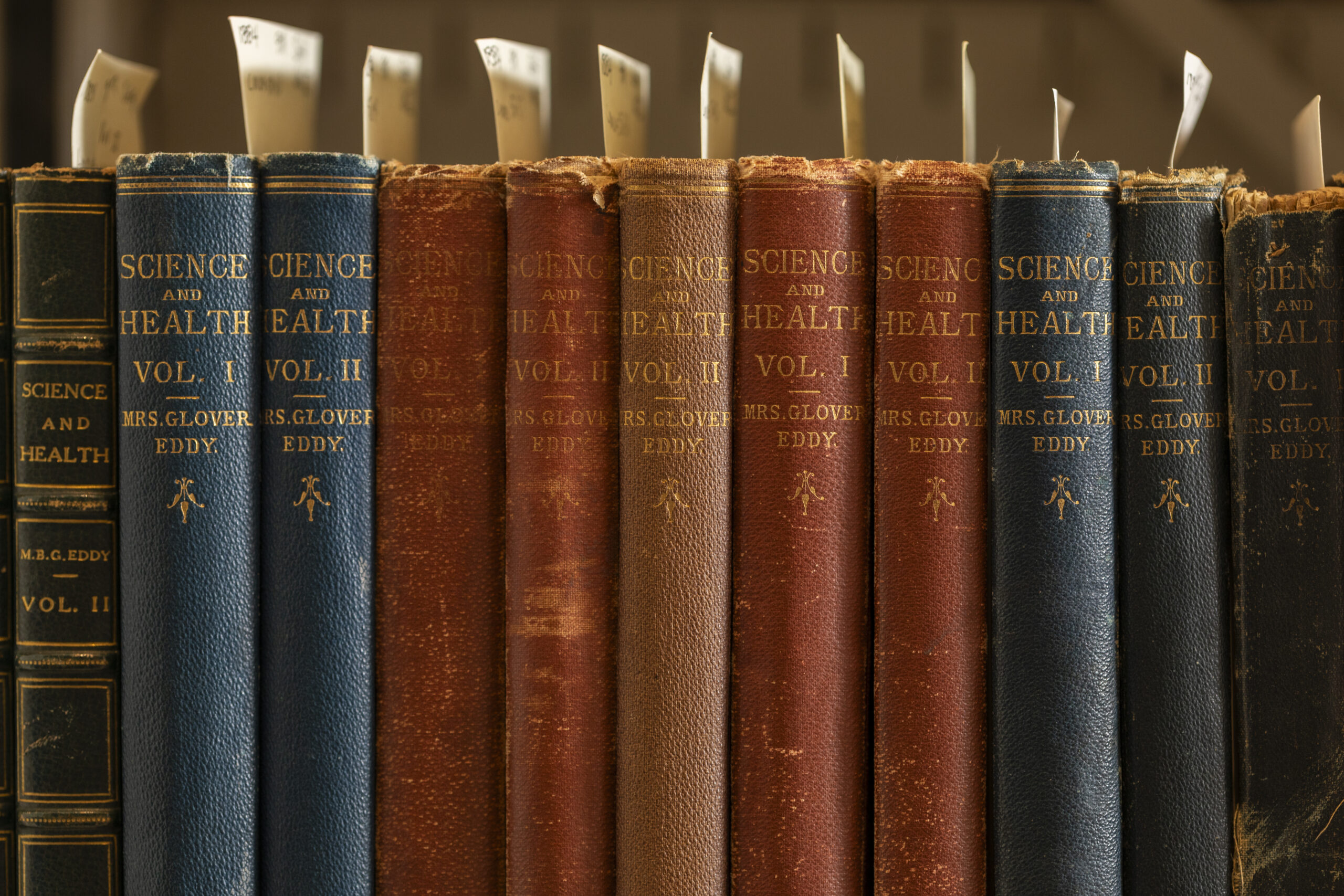 Multiple early edition copies of Science and Health with Key to the Scriptures on a shelf.