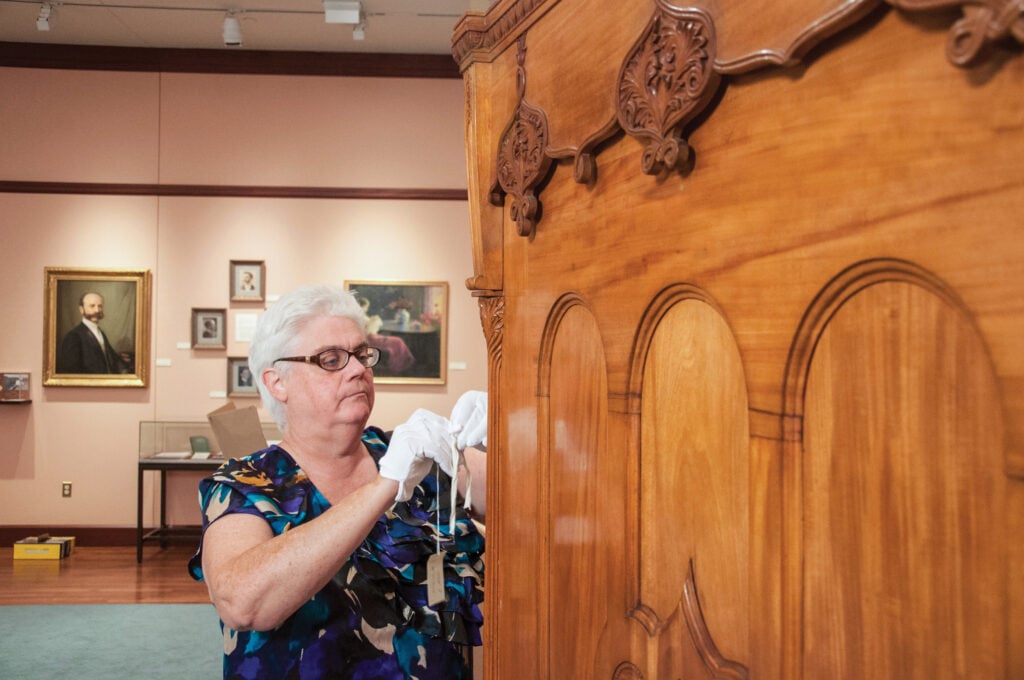 Leslie Vollnogle attaches a tag to a Murphy bed owned by Mary Baker Eddy for Longyear Museum.
